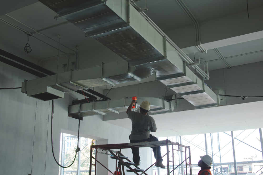 man on scaffolding installing overhead ventilation ducts in factory environment