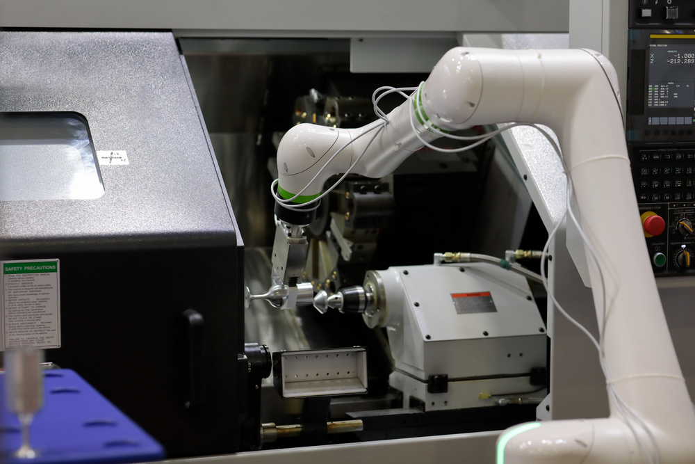 A robot arm is machine tending. The robot is reaching into a CNC machine to remove a workpiece.