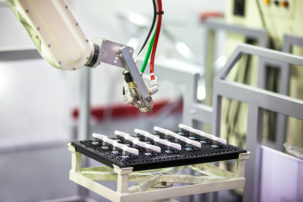 Painting robot poised to apply coating to small plastic parts in a tray