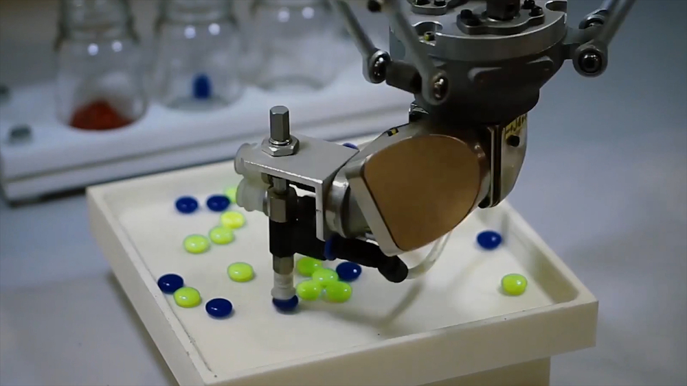 A SCARA robot is picking and placing green and blue tablets in a pharmaceutical production application.
