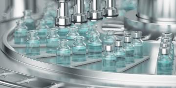 Pharmaceutical robotics handle small glass bottles containing liquid in a high-volume production environment.