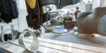 A robotic arm performs a deburring operation on a metal workpiece in a factory environment. 