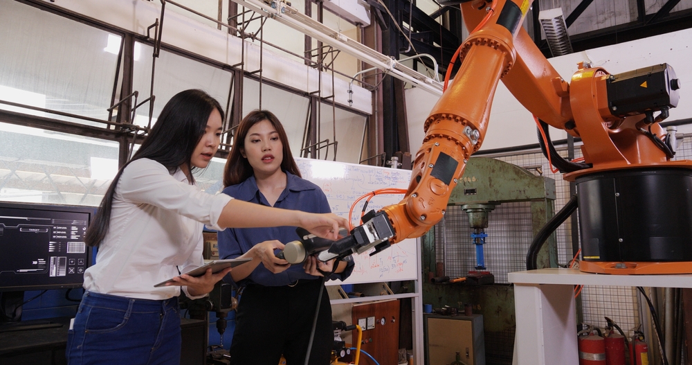 A picture of a collaborative robot, or cobot, with two female engineers in a factory environment