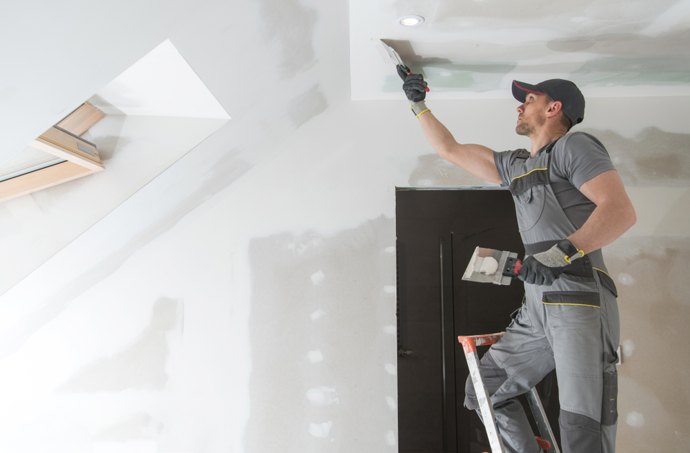 man on a ladder applying mud for drywall